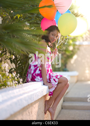 Stati Uniti d'America, Arizona, Scottsdale, giovane donna sorridente seduto sul muro e palloncini di contenimento Foto Stock