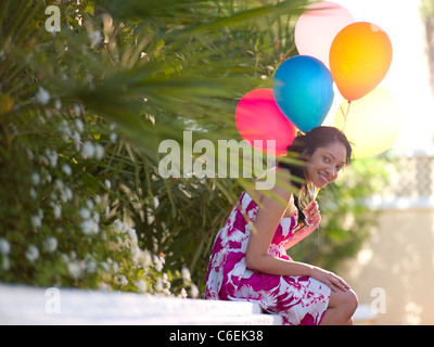 Stati Uniti d'America, Arizona, Scottsdale, giovane donna sorridente seduto sul muro e palloncini di contenimento Foto Stock