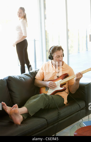 Uomo maturo a suonare la chitarra donna in piedi accanto alla finestra Foto Stock