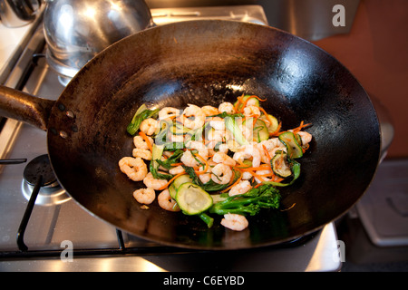Lo stile orientale di mescolare verdure fritte e gamberoni in un wok, Londra Foto Stock