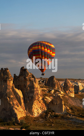 Colorato arlecchino i palloni ad aria calda sul basso livello di volo attraverso la Cappadocia cime calcaree terreno early morning sun Foto Stock