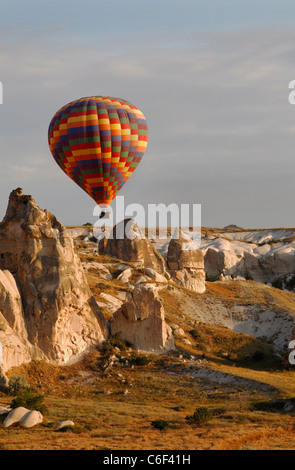 Colorato arlecchino i palloni ad aria calda sul basso livello di volo attraverso la Cappadocia cime calcaree terreno early morning sun Foto Stock