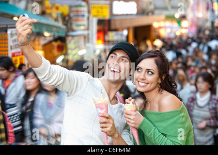 Giocoso giovane prende un autoritratto mentre mangiando crepes nel centro cittadino di Tokyo di notte. Foto Stock