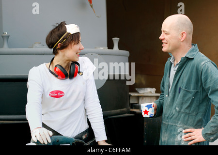 Un uomo e una donna in chat durante una pausa, mentre lavora su alcuni la levigatura per l'interno di un narrowboat. Indossando i DPI. Foto Stock