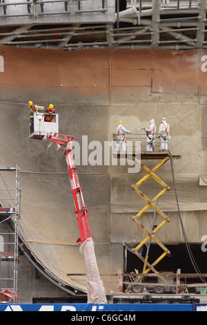 Lavoratori edili verticale utilizzando piattaforme di sollevamento che indossa caschi di sicurezza e indumenti protettivi Foto Stock