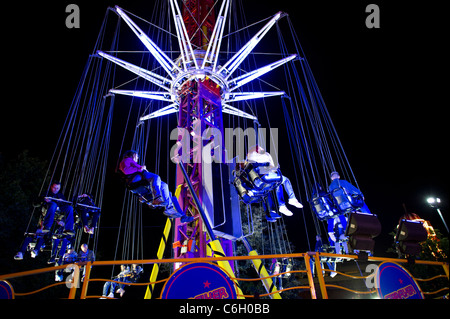 La gente seduta su una illuminazione fairground ride di notte. Foto Stock