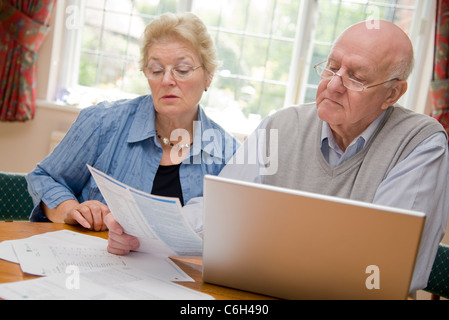 Coppia matura passando attraverso le loro bollette e conti insieme online Foto Stock