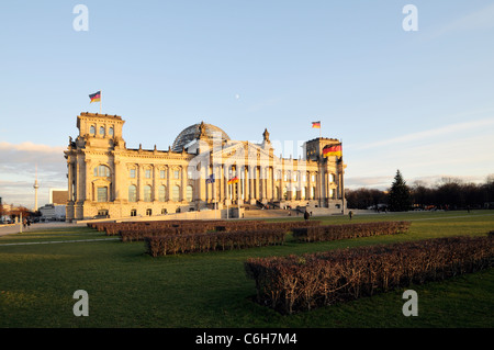 Serata calda luce del sole illumina il possente Palazzo del Reichstag con cielo azzurro e bandiere. Foto Stock