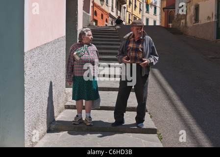 Un anziana coppia italiana parla e gesto come essi camminare sul marciapiede nel loro villaggio di Riomaggiore, Cinque Terre, Italia.