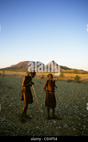 Himba uomini in arido paesaggio, uno di fumare un tubo Foto Stock