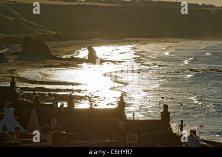 Cullen Beach- Moray Coast in fine di sun con rock e case in profilo Foto Stock