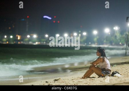 Donna thai indossando vestiti bagnati seduto sulla sabbia in spiaggia di Pattaya di notte, Pattaya , Thailandia Foto Stock