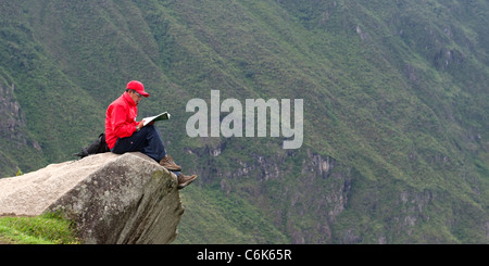 Persona la lettura di un libro in corrispondenza del bordo di una roccia presso la cittadella Inca di Machu Picchu, regione di Cusco, Perù Foto Stock