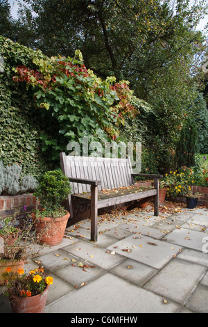 Un informale giardino inglese in autunno con il tradizionale panca in legno, piastrelle in terracotta e vasi per piante Foto Stock