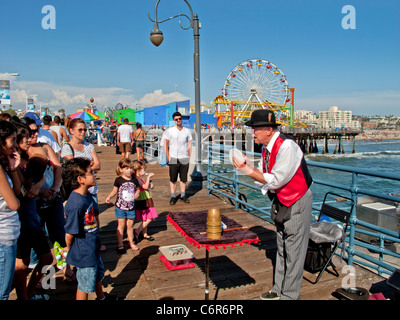 Un anziano mago rimescola le carte per il suo pubblico nel parco di divertimenti sul molo di Santa Monica. Foto Stock