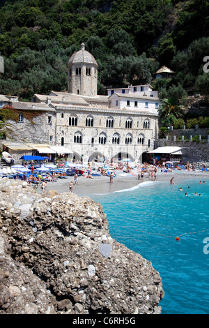 Vista di San Fruttuoso di Camogli, Liguria, Italia, con abbazia medievale, vecchi edifici, mare blu, spiaggia rocciosa e la gente di nuoto Foto Stock