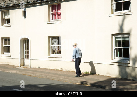 Un uomo anziano a piedi attraverso il villaggio di Mickleton, Gloucestershire, England, Regno Unito Foto Stock