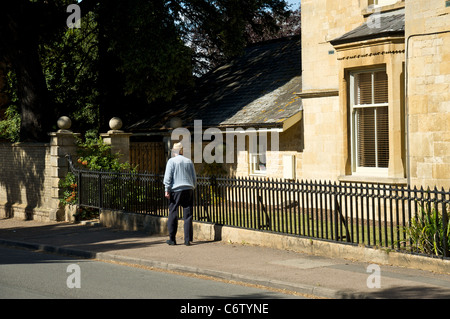 Un uomo anziano a piedi attraverso il villaggio di Mickleton, Gloucestershire, England, Regno Unito Foto Stock