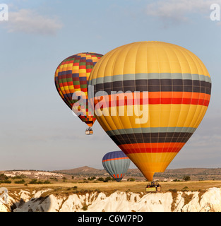 Tre colorato i palloni ad aria calda a basso livello di volo su Cappadocia cliffs, early morning sun, formato quadrato, cielo blu, il raccolto s Foto Stock
