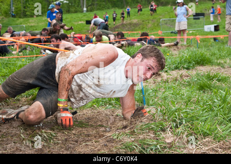 Un robusto Mudder crawl del partecipante attraverso il "Kiss il fango " sezione del corso. Mudder dura una giornata di sport estremi Foto Stock