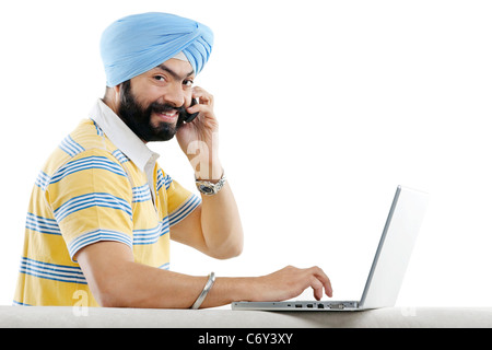 La religione Sikh l uomo a parlare al telefono mentre si lavora su un computer portatile Foto Stock