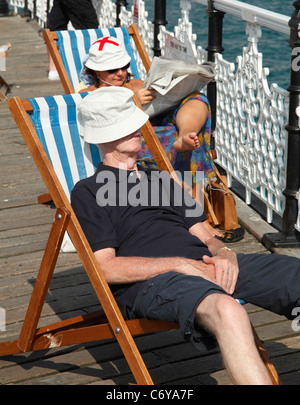 I vacanzieri in rilassanti sedie a sdraio sul molo di Brighton, Brighton, Inghilterra, Regno Unito Foto Stock