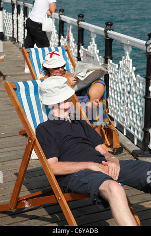 Persone in rilassanti sedie a sdraio sul molo di Brighton, Brighton, Inghilterra, Regno Unito Foto Stock