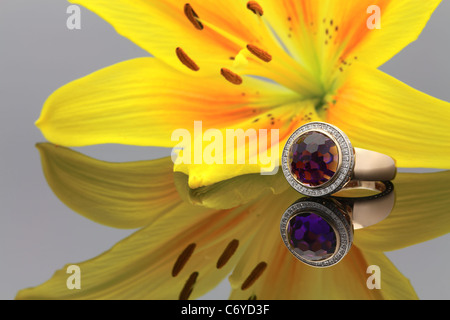 Anello d'oro con una grande gemma sulla superficie di mirroring e un grande giglio giallo su uno sfondo Foto Stock