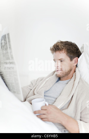 Uomo che legge il giornale in bed Foto Stock