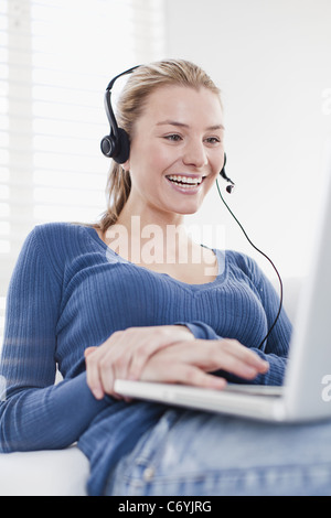 Donna che utilizza la cuffia sul computer portatile Foto Stock