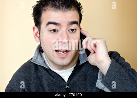 Un giovane uomo che parla sul suo telefono cellulare con una occhiata interessata sul suo volto. Foto Stock