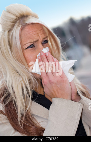 Questa giovane donna di starnuti ripetuti in un tessuto o ha un raffreddore o veramente male le allergie. Foto Stock