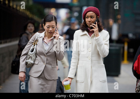 Due donne di business avente le conversazioni sui loro telefoni cellulari mentre si cammina in una grande città. Foto Stock
