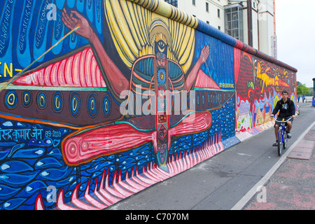 La parte restante pezzo dipinto del muro di Berlino in Germania uomo ragazzo ciclo di bicicletta pedalando attraverso il colore colorato colorato Foto Stock