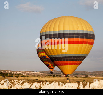 Due i palloni ad aria calda volare basso livello vicino a una scogliera, multicolorata arlecchino e giallo con bande colorate, early morning sun Foto Stock