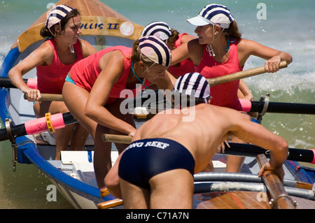 La femmina (equipaggio e timoniere maschio) di un surf barca di salvataggio andare all'inizio di una gara durante un carnevale di surf. Foto Stock