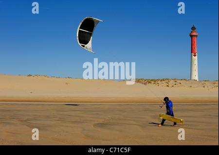 Uomo che cammina su una spiaggia di sabbia in possesso di un kite surf vicino a un faro, Charente Maritime, a ovest della Francia Foto Stock