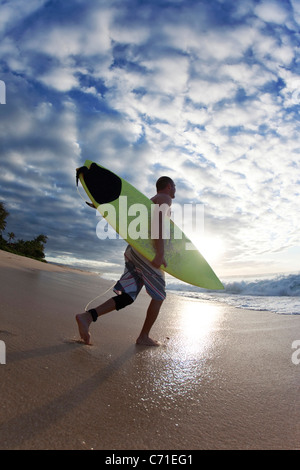 Giovane uomo a camminare per il surf a Rocky Point sulla North Shore di Oahu, Hawaii.