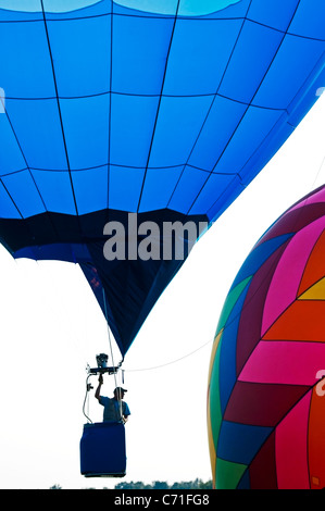 Un uomo in mongolfiera ad aria calda salendo con pilota stagliano contro un cielo luminoso. Foto Stock