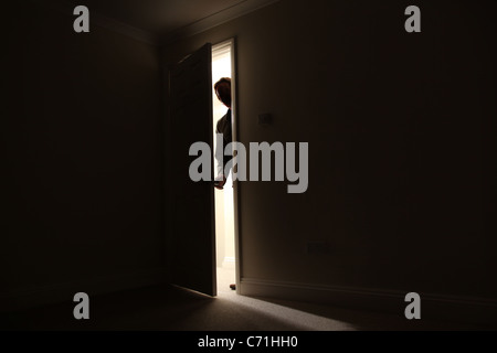 Silhouette di un maschio in piedi al di fuori di una stanza buia in Cerca in. Foto Stock