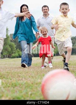 Famiglia sportiva giocando a calcio sul prato verde su sfondo naturale Foto Stock