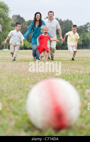 La famiglia felice di cinque avente all'aperto e giocare a calcio in marcia verso il calcio su sfondo naturale Foto Stock
