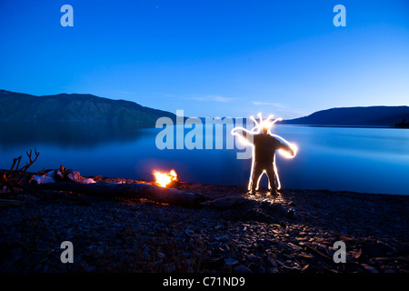 Una creatura sorge accanto a un falò e il lago in Sandpoint, Idaho. Questa luce pittura immagine è stata creata con una lunga esposizione di un Foto Stock