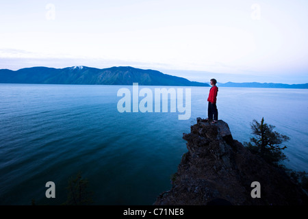 Un uomo bello pacificamente sorge sul bordo di una scogliera a guardare il sole sorgere sopra il lago in Idaho. Foto Stock