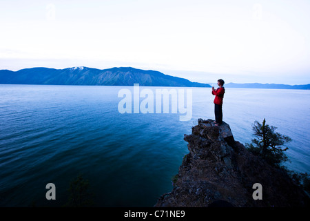 Un uomo bello pacificamente sorge sul bordo di una scogliera a guardare il sole sorgere sopra il lago in Idaho. Foto Stock