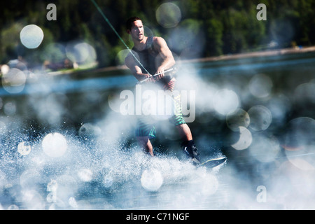 Un felice uomo atletico wakeboarding scolpisce in una giornata di sole in Sandpoint, Idaho. Foto Stock