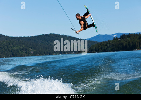 Un uomo atletico wakeboard salti enormi sopra la scia e le montagne in Idaho. Foto Stock