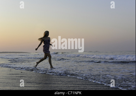 Una giovane donna corre nel surf durante il tramonto. Foto Stock