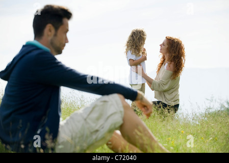 Madre di parlare con la giovane figlia all'aperto, padre guardando dal primo piano Foto Stock