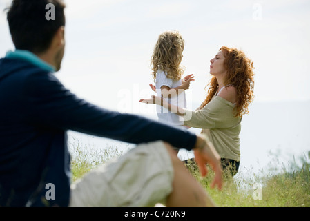 Madre di parlare con la giovane figlia all'aperto, padre guardando dal primo piano Foto Stock